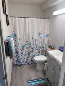 Brightly lit full bathroom with floral shower curtain.